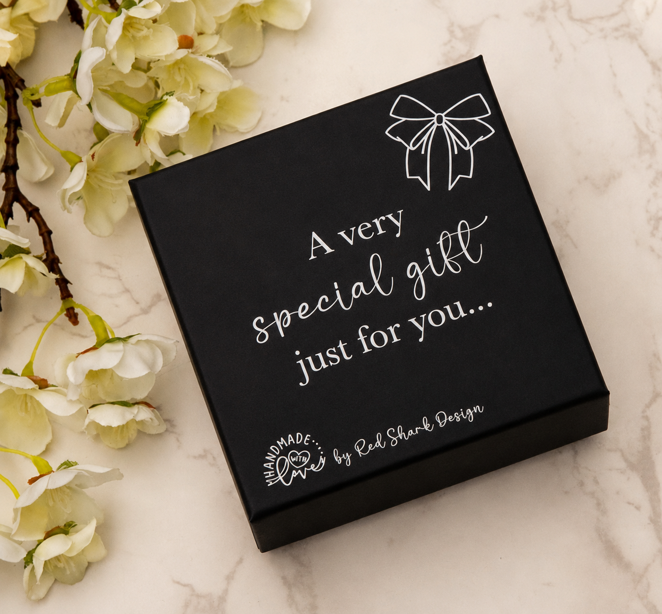 Black gift box with white text on a marble surface with flowers