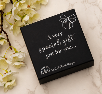 Black gift box with white text on a marble surface with flowers