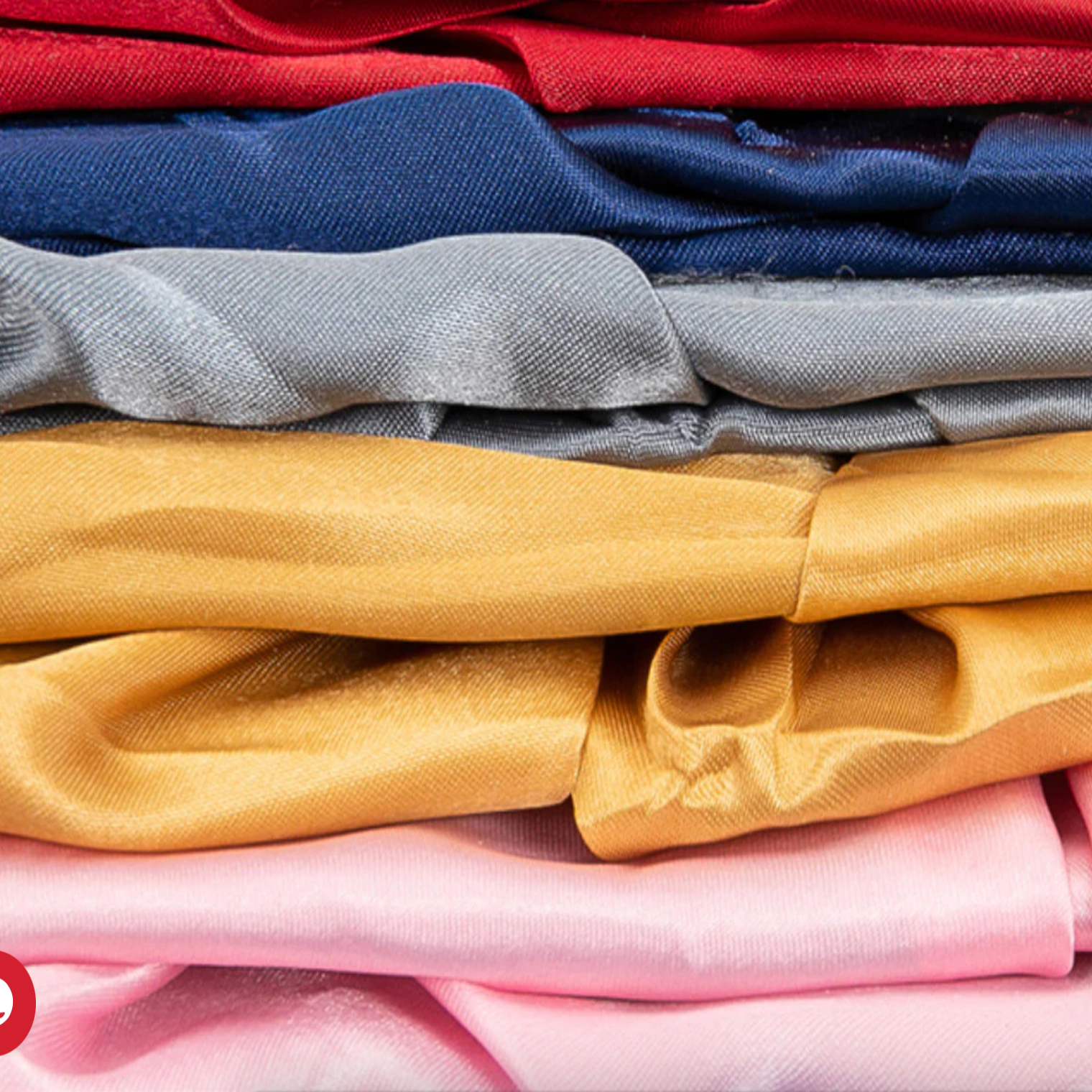 Stack of folded colourful silk fabric in red, blue, silver, gold and pink.