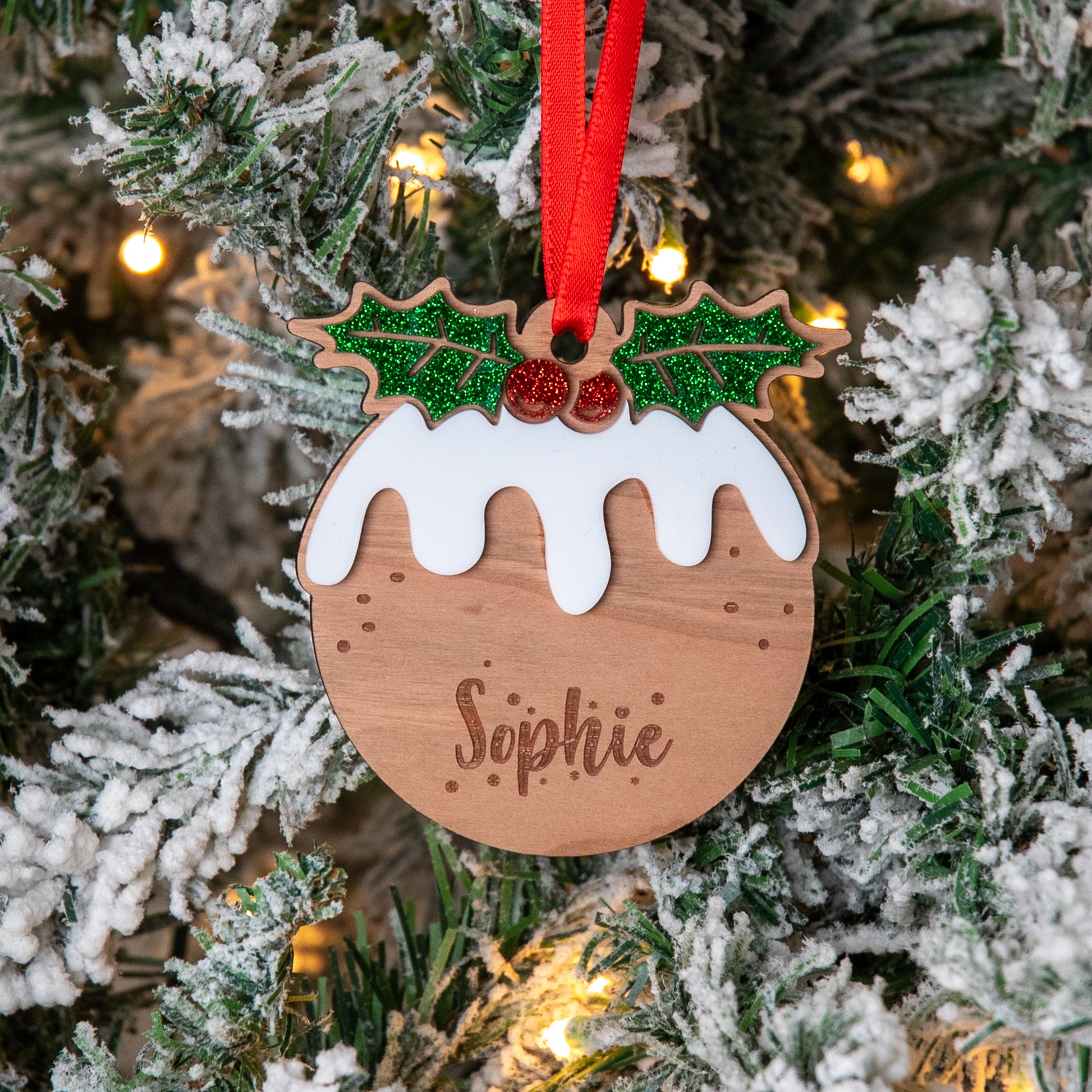 Wooden Christmas ornament shaped like a pudding with holly leaves and berries, hanging on a decorated tree.