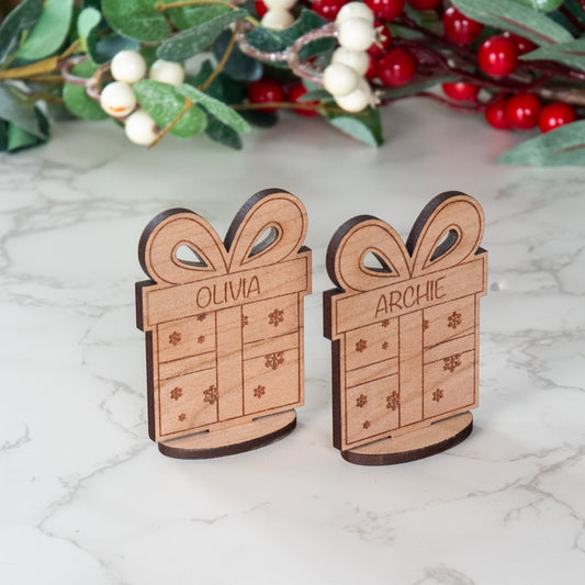 Two wooden gift box ornaments with names 'Olivia' and 'Archie' on a marble surface with decorative berries in the background.