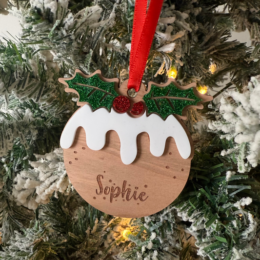 Wooden Christmas ornament shaped like a pudding with holly leaves and berries, hanging on a tree.
