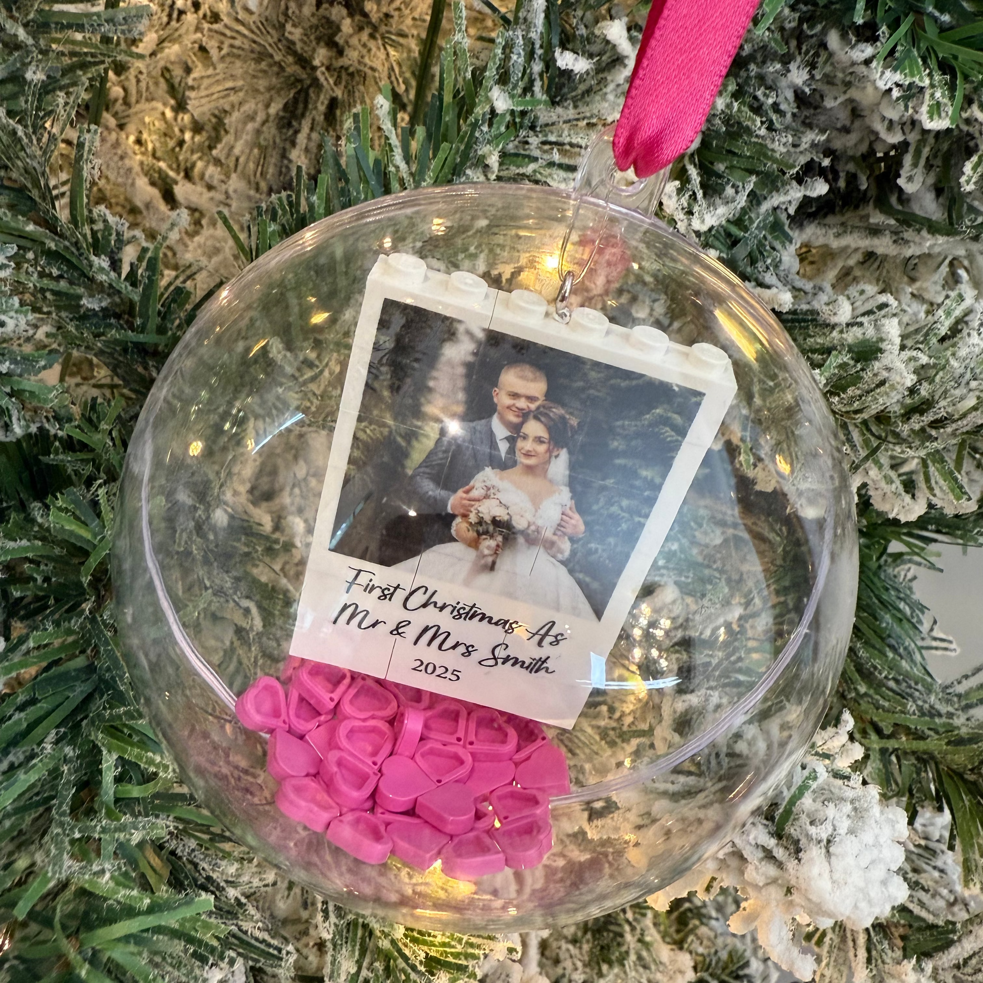 Christmas ornament with a photo of a couple and pink decorations on a tree.