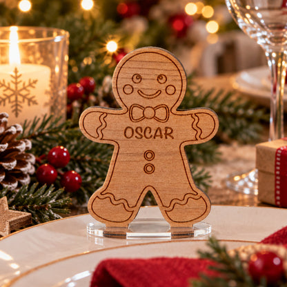 A personalized wooden gingerbread man table sign engraved with the name 'OSCAR' stands on a clear acrylic base on a decorated Christmas table setting.