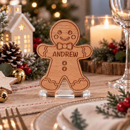 A personalized gingerbread man table place card with the name 'ANDREW' engraved on the chest, displayed on a decorated Christmas table setting with candles, pinecones, and holiday greenery.